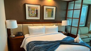 A hotel room with a large bed, two bedside lamps, a nightstand, a chair, and artwork on the wall. - MGM Signature | No Resort Fees, Jacuzzi & Pools (Las Vegas)