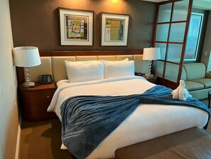 A hotel room with a large bed, two bedside lamps, a nightstand, a chair, and artwork on the wall.
