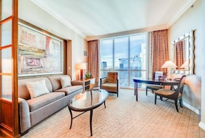 A hotel room with a sofa, armchair, dining table, and chairs.