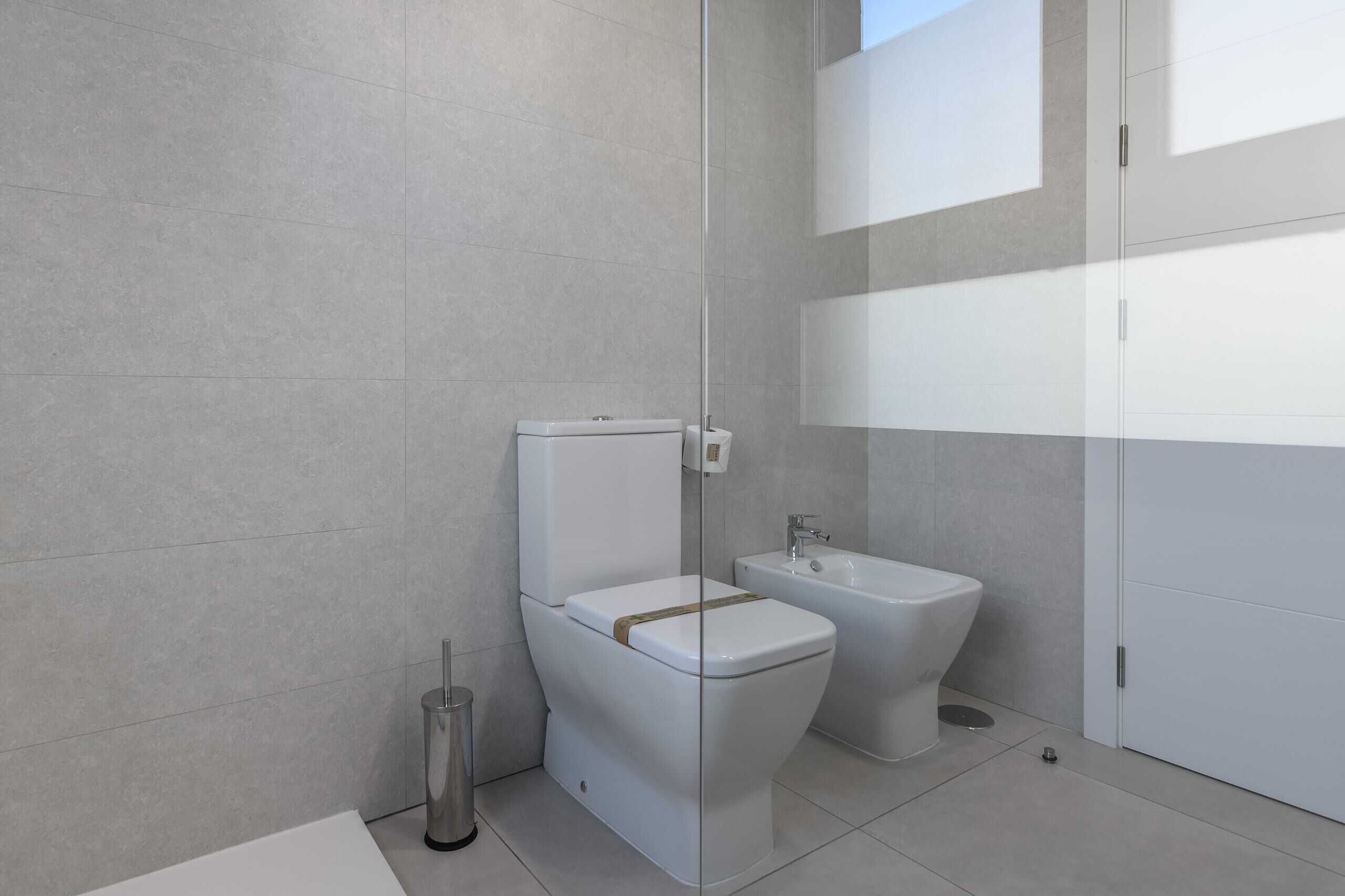 A modern bathroom with a toilet, bidet, and a glass shower enclosure.