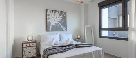 A bedroom with a bed, bedside table, lamp, and a window with a view.