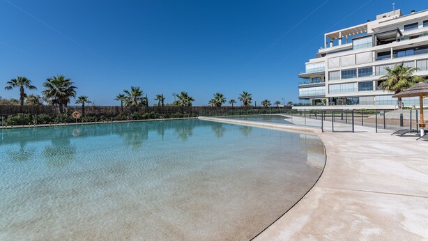 Un hôtel moderne doté d’une grande piscine, de palmiers et surplombant un ciel d’un bleu éclatant.