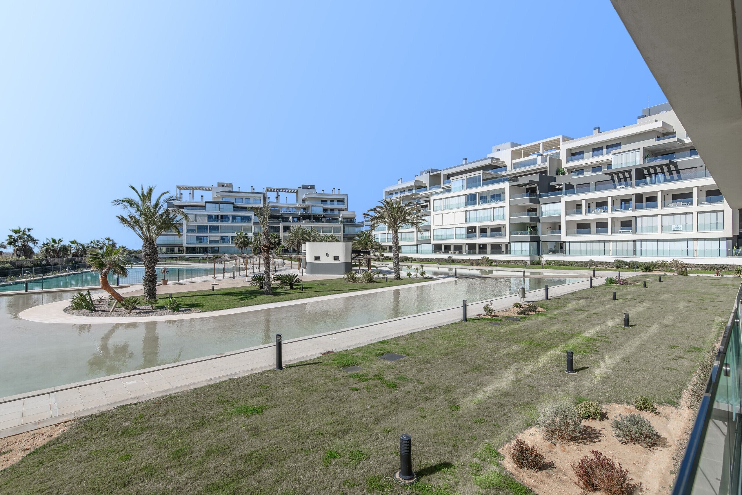 Un hotel moderno con varias plantas, piscina y una zona ajardinada con palmeras.