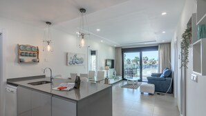 Une cuisine moderne avec un îlot central, un coin repas doté d’une table en verre et un salon avec un canapé bleu.