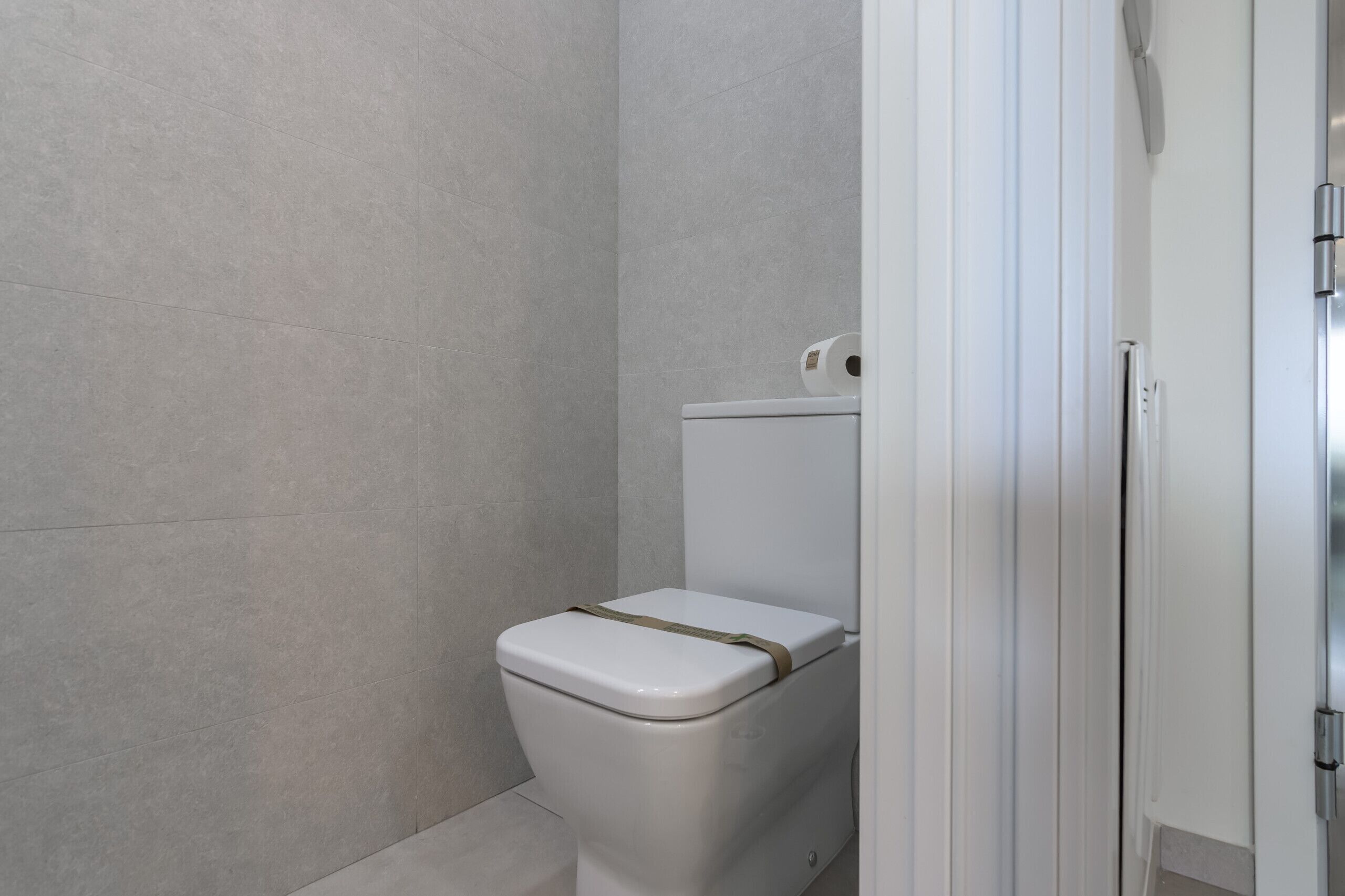 A bathroom with a white toilet, a roll of toilet paper on the tank, and a shower area.