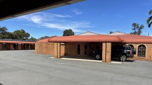 Un edificio de fachada de ladrillo, con una zona de estacionamiento techada y un vehículo negro estacionado en su interior.