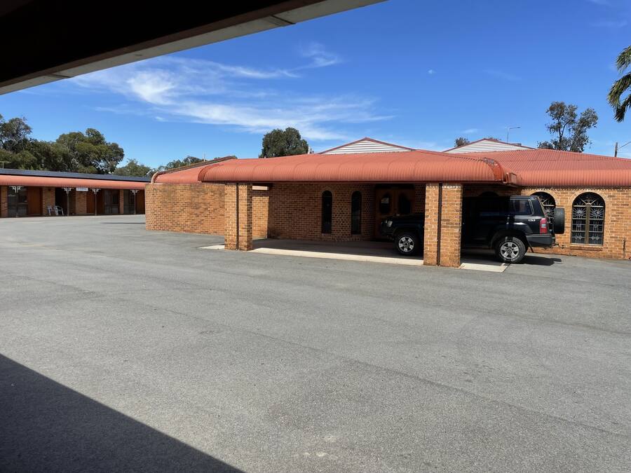 A building with a brick facade, a covered parking area, and a black vehicle parked inside.