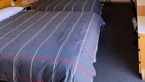 Habitación de hotel con dos camas, un escritorio, sillas, ventilador de techo y pared de ladrillo.