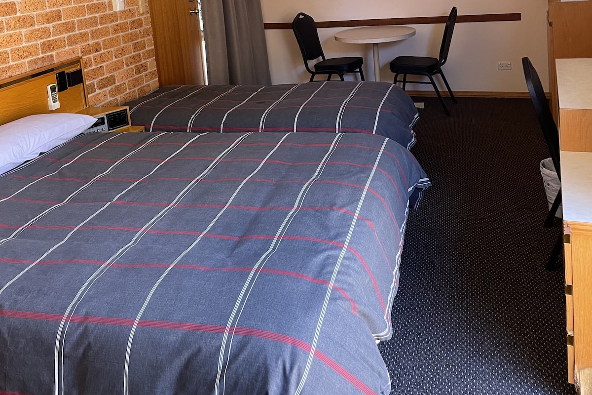 Ein Hotelzimmer mit zwei Betten, einem Schreibtisch, Stühlen, einem Deckenventilator und einer Ziegelwand.