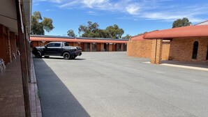 Un edificio con fachada de ladrillo y tejado rojo, un estacionamiento pavimentado y una camioneta negra estacionada al frente.