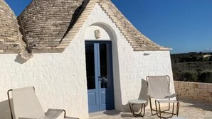 A white building with a blue door and a stone roof, featuring a hot tub and two chairs. - Borgofreddo (Monopoli)