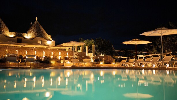 A nighttime pool area with lounge chairs and umbrellas, reflecting the lights. - Borgofreddo (Monopoli)
