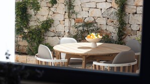 A stone wall with climbing plants, a round wooden table with chairs, and a bowl of fruit. - Borgofreddo (Monopoli)
