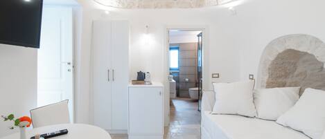A modern bedroom with a stone ceiling, a bed with white bedding, a small table with a remote and a vase, and a white wardrobe.