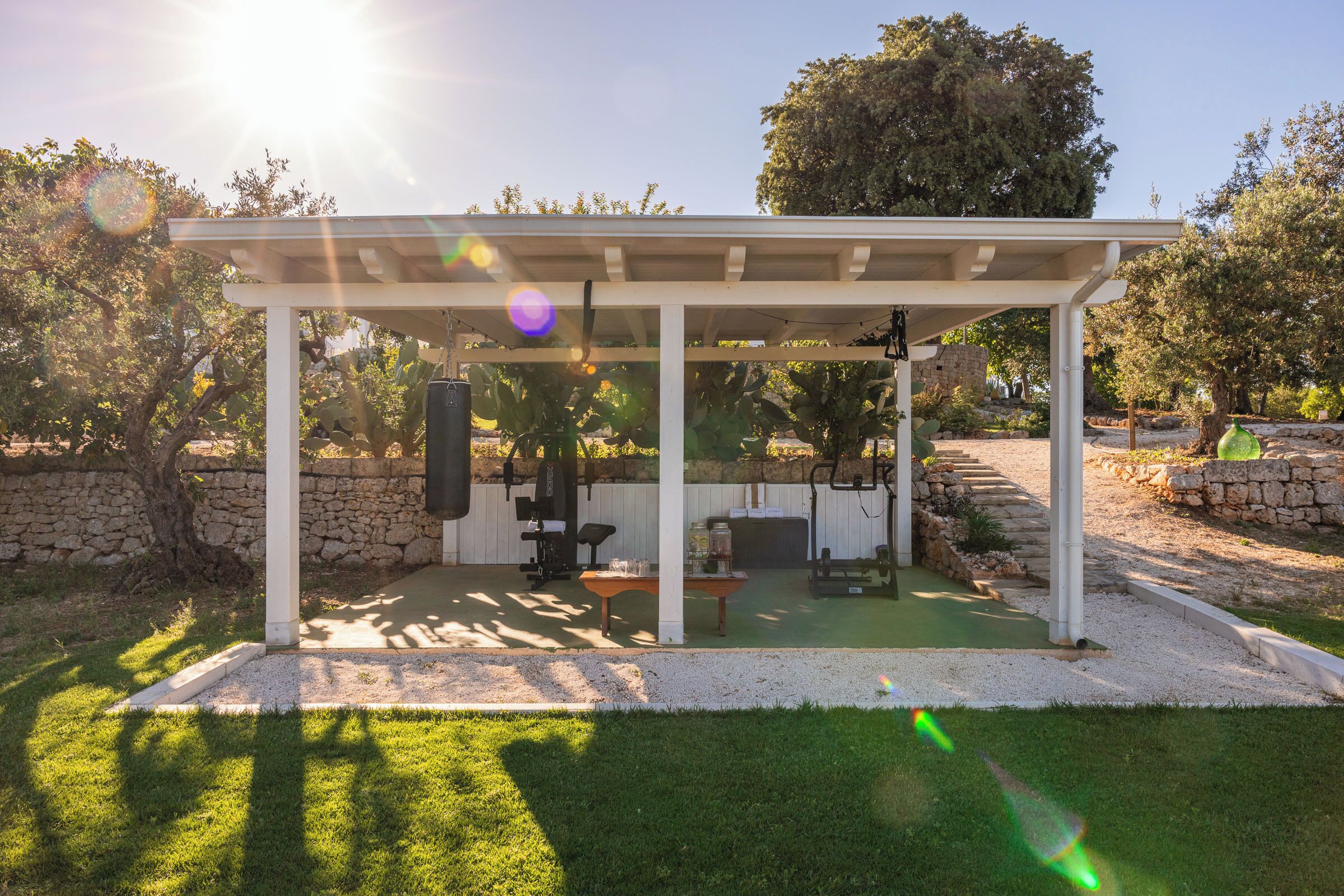 A covered outdoor area with a barbecue grill, exercise equipment, and a stone wall.