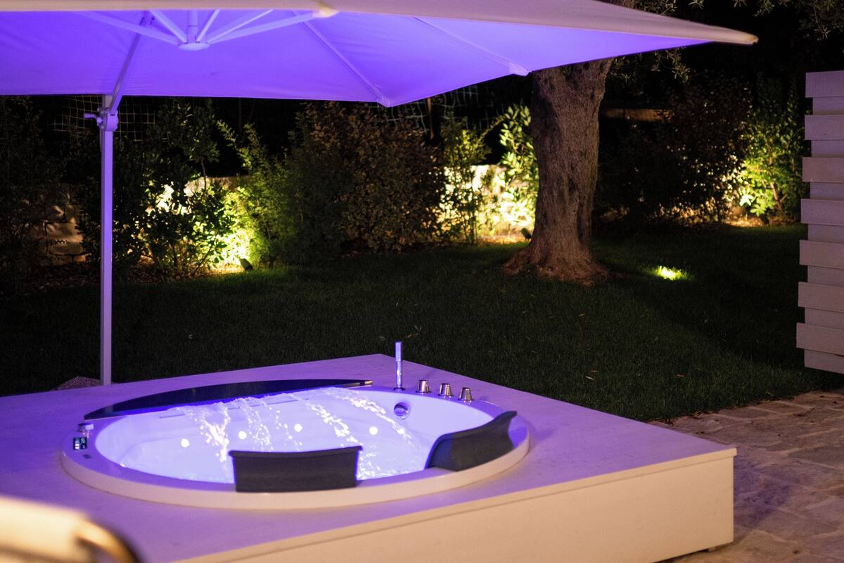 A hot tub with an umbrella, surrounded by a stone patio and a tree.