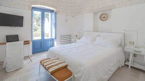 A bedroom with a large bed, a desk with a computer, a TV mounted on the wall, and a door leading outside. - Borgofreddo (Monopoli)