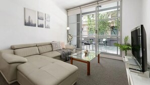 A modern living room with a beige sofa, a glass coffee table, and a flat-screen TV. - A Modern & Comfy Studio Next to Darling Harbour (Sydney)