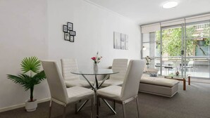 A modern living room with a glass dining table surrounded by four chairs, a sofa, and a potted plant. - A Modern & Comfy Studio Next to Darling Harbour (Sydney)