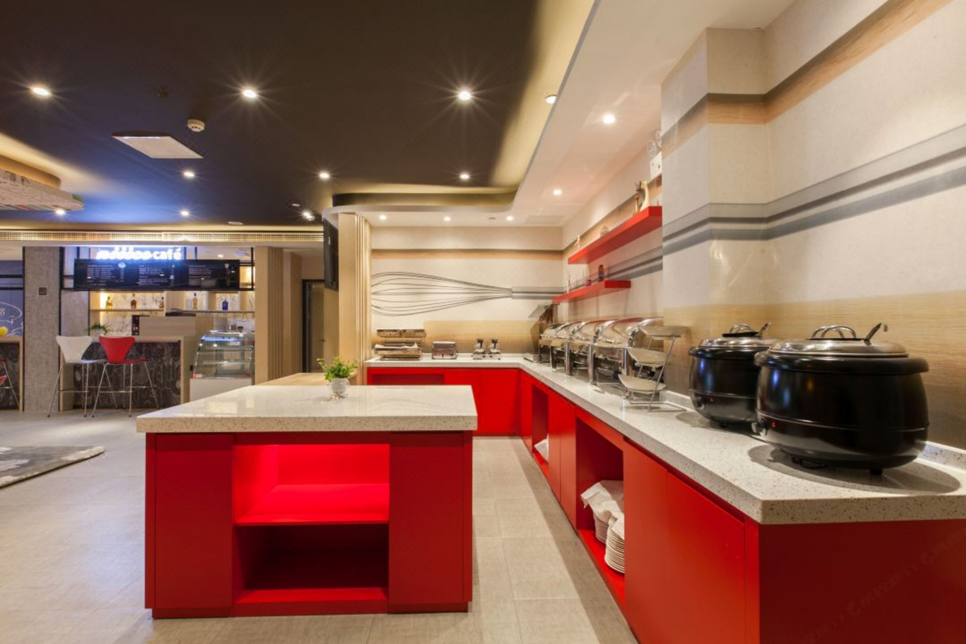 A modern kitchen with a red accent island, stainless steel appliances, and a coffee bar in the background.