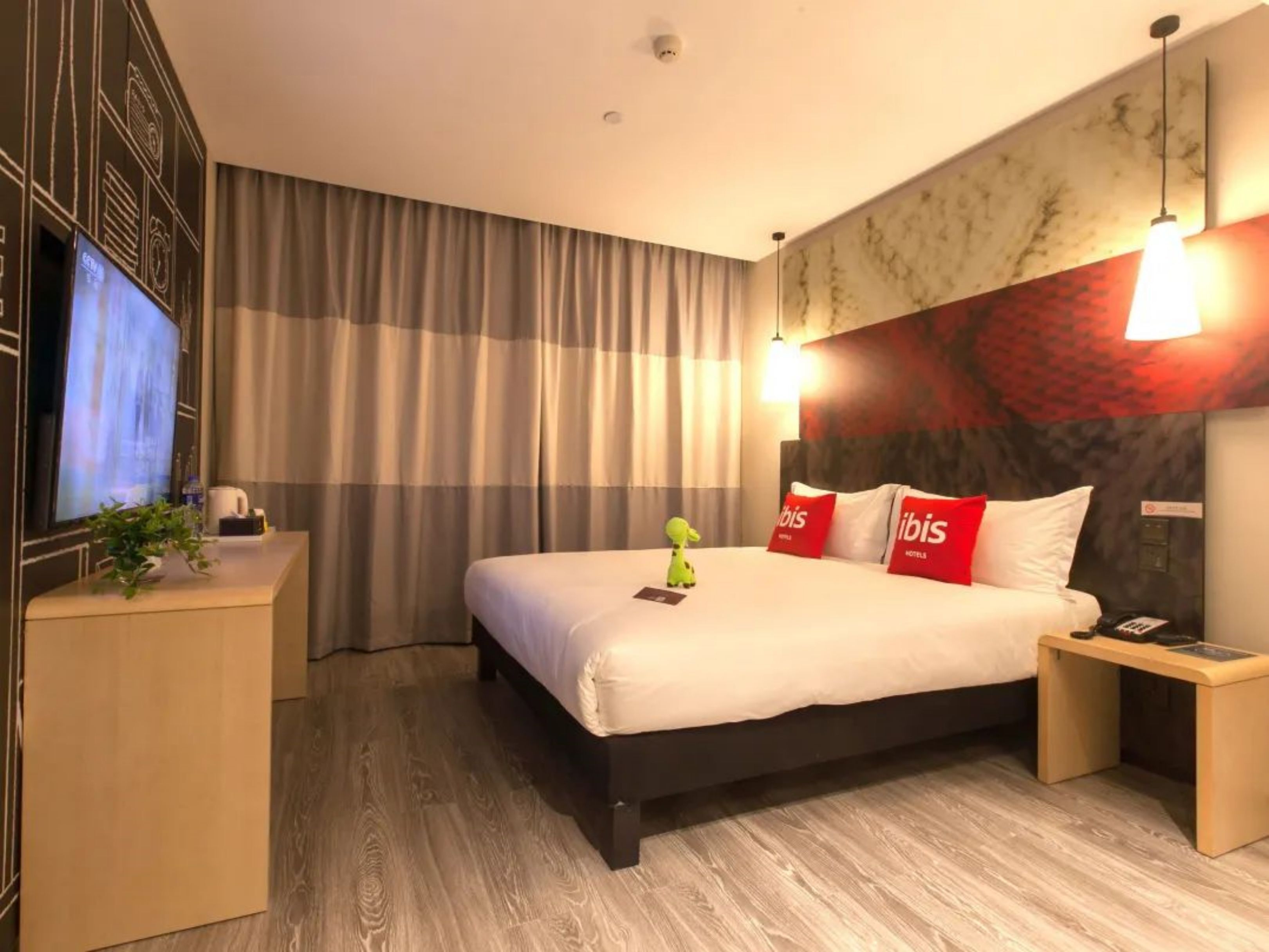 Ein Hotelzimmer mit einem großen Bett, einem Nachttisch, einem Fernseher und einem Schreibtisch mit Pflanze.