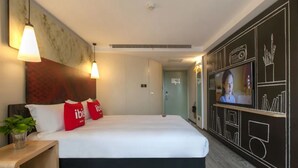 Une chambre d’hôtel avec un grand lit, deux lampes de chevet, un téléviseur fixé au mur et un mur décoratif orné de motifs géométriques.