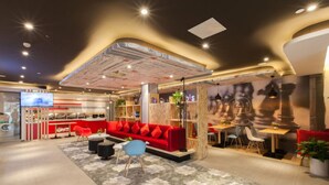 Un hall d’hôtel moderne avec un canapé rouge, un coin bar et un espace repas.