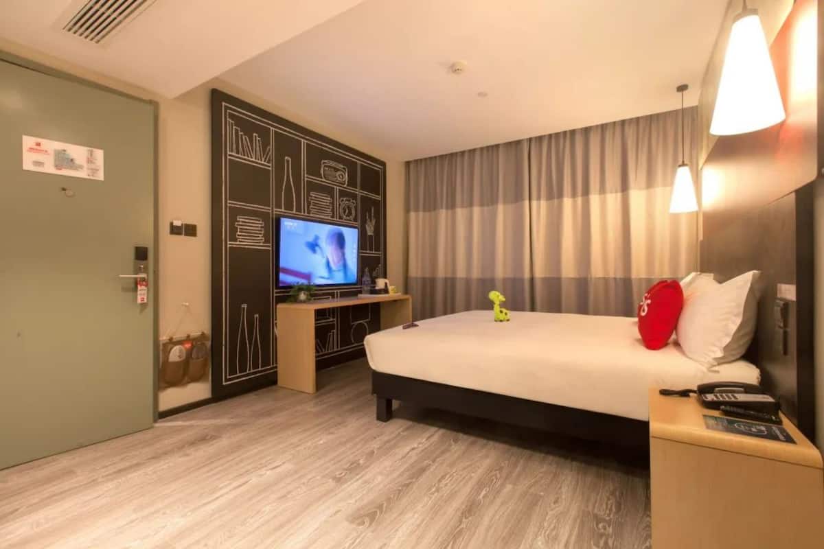A hotel room with a bed, a TV, a desk, and a curtain.