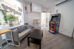 Un interior moderno con un sofá, una mesita, una máquina de videojuegos y un cartel que indica un baño.