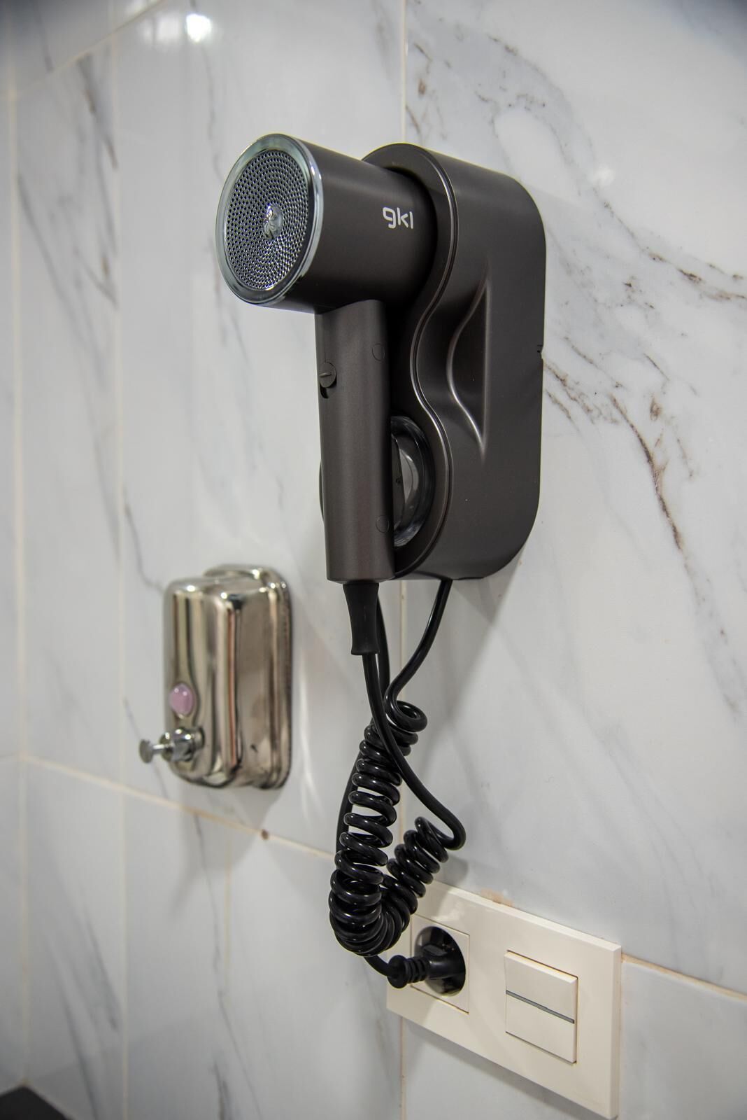 Un sèche-cheveux fixé au mur, avec un cordon enroulé.