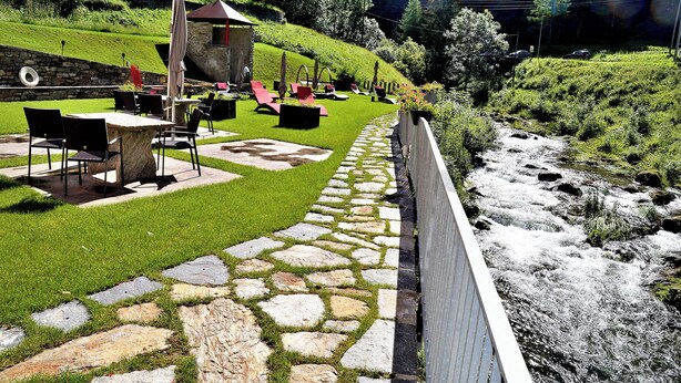 A patio with stone flooring, outdoor seating, and a view of a flowing river. - Boutique Hotel Fusio (Lavizzara)