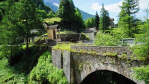 A stone bridge over a river with houses on the opposite bank, surrounded by greenery and mountains in the background. - Boutique Hotel Fusio (Lavizzara)