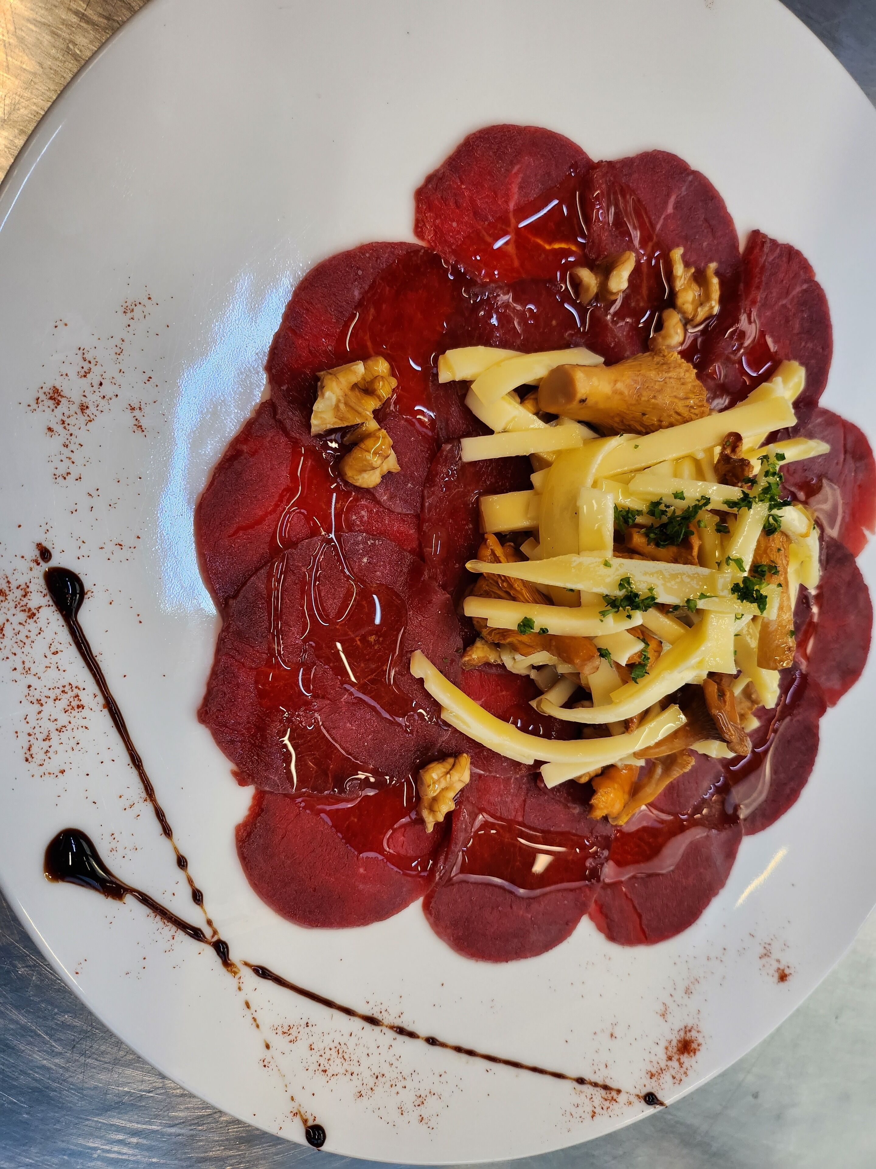 A plate of food with sliced meat, nuts, cheese, and herbs.