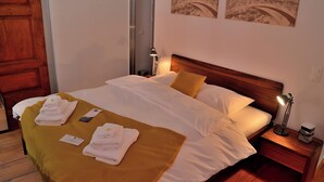A neatly made bed with white linens and a mustard-colored throw, a bedside lamp, and a small nightstand with a lamp and a cup. - Boutique Hotel Fusio (Lavizzara)