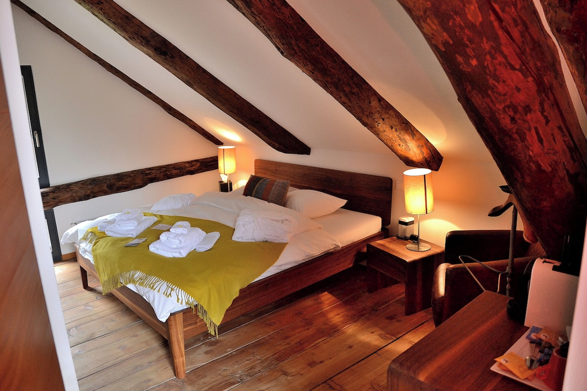 Um quarto acolhedor com uma cama de madeira, duas luminárias de cabeceira e um banquinho de madeira.