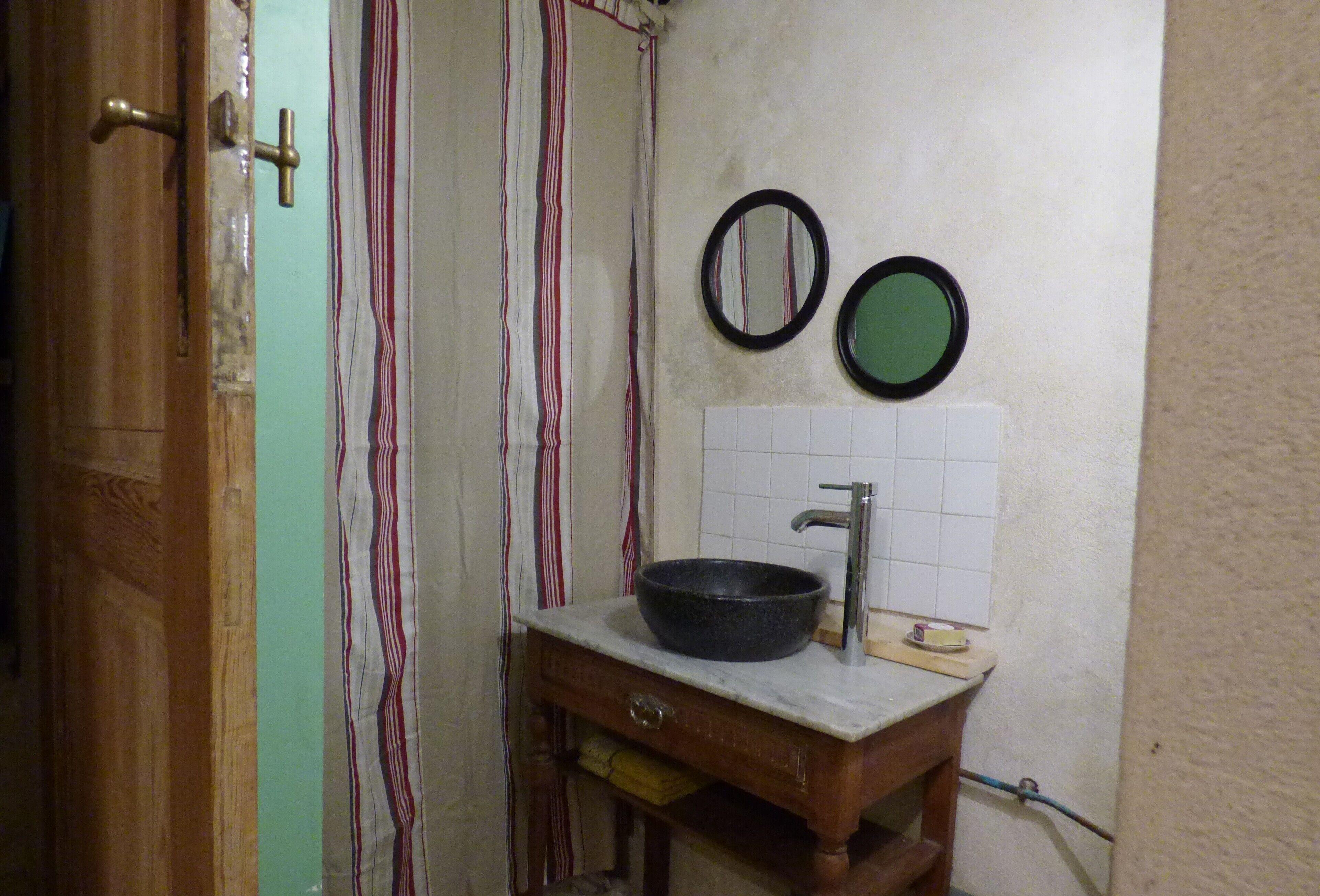 Ett badrum med ett handfat i trä, en svart tvättställsskål, två speglar som är monterade på väggen och en randig gardin.