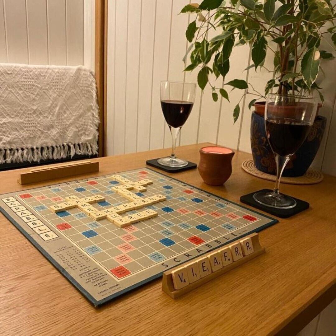 A Scrabble board game on a wooden table with a plant and two wine glasses.