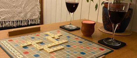 A Scrabble board game on a wooden table with a plant and two wine glasses.
