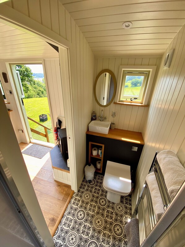 A compact bathroom with a toilet, sink, and mirror. It features a small window and a view of the outdoors. - A quiet and cosy Shepherds Hut, with wood burning fire with scenic views (Conwy)