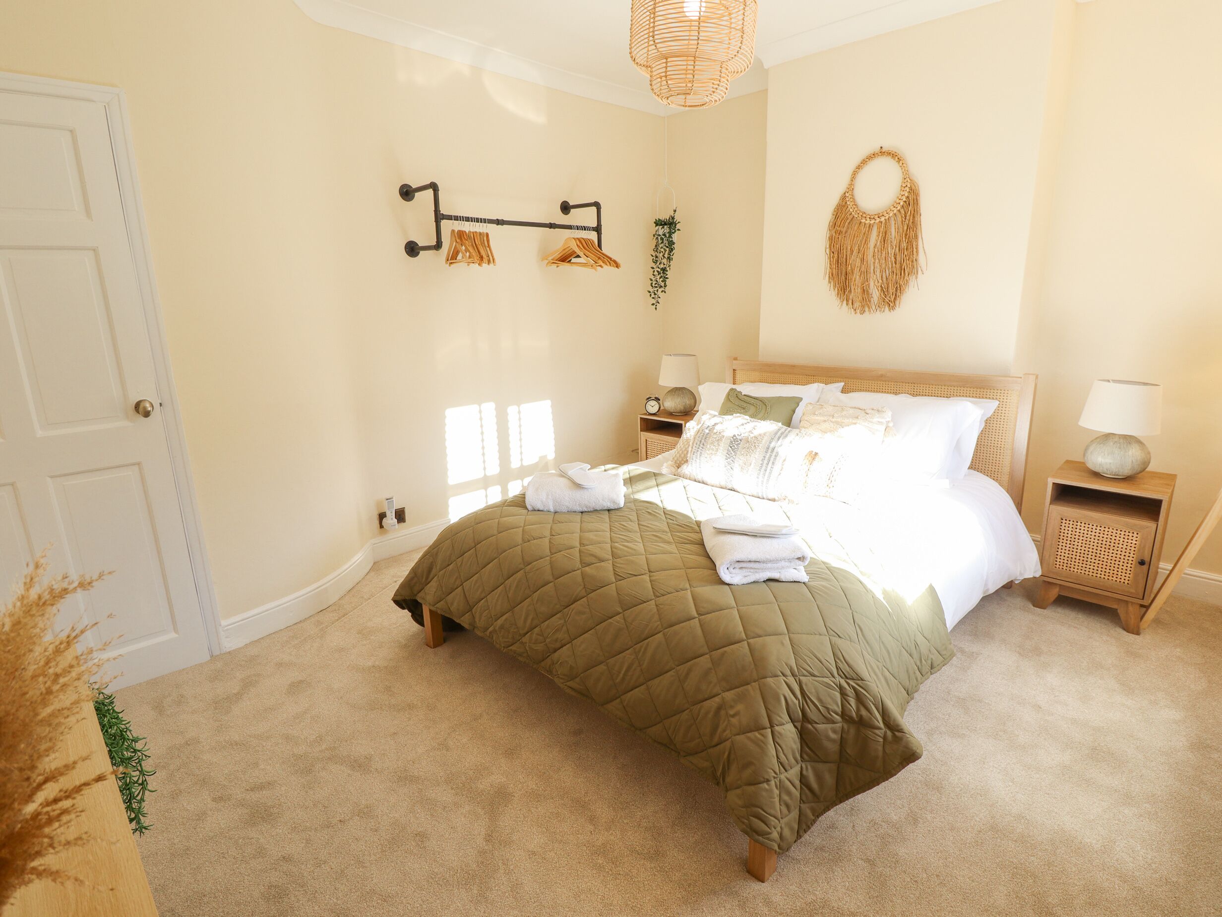 A bedroom with a bed, bedside tables, a wall-mounted towel rack, and a hanging macrame wall decoration.