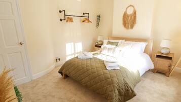 A bedroom with a bed, bedside tables, a wall-mounted towel rack, and a hanging macrame wall decoration.