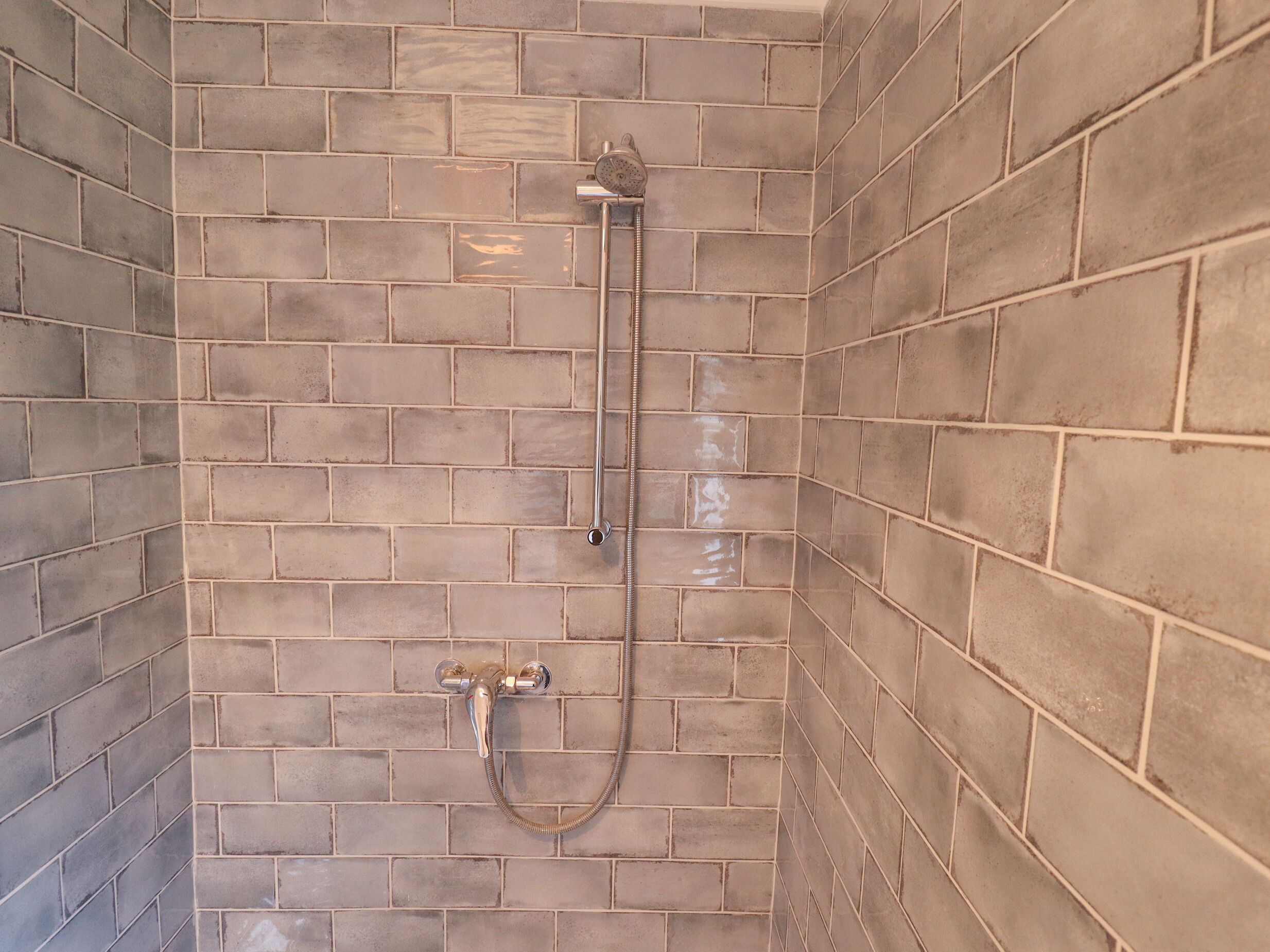 Un área de ducha con pared de azulejos, un cabezal de ducha manual y un grifo empotrado.