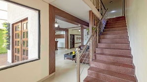 A spacious hallway with a staircase leading to an upper floor. The hallway features large windows, a wooden door, and a tiled floor. - Treebo Maurice (Baddi)