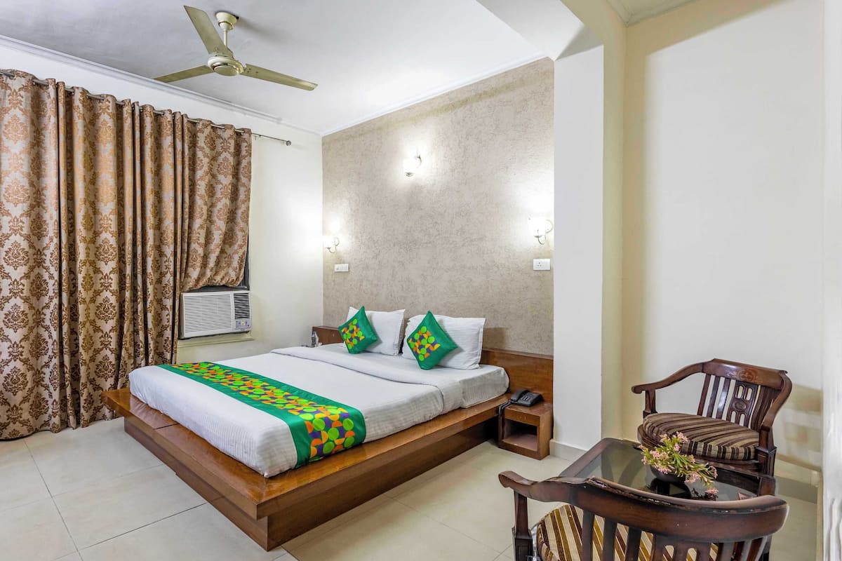 A hotel room with a bed, a chair, a table, and a ceiling fan.