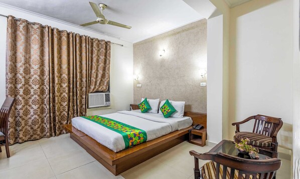 A hotel room with a bed, a chair, a table, and a ceiling fan.