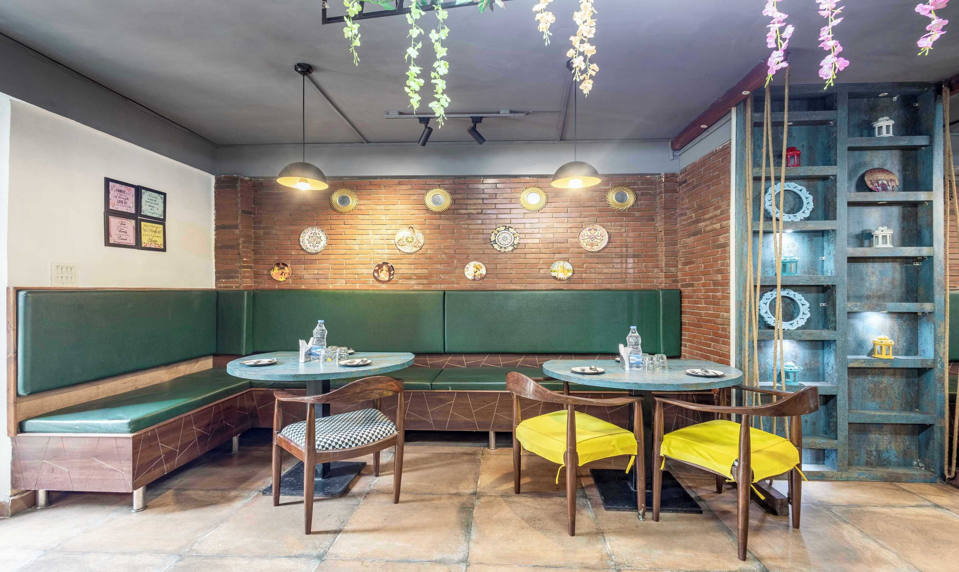 Ein Restaurantinneres mit grünen Sitzbänken, Holztischen und hängenden Pflanzen.