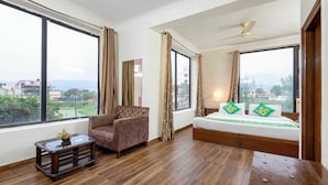 A hotel room with a large bed, a chair, a small table with a plant, and large windows offering a view of the city. - Treebo Maurice (Baddi)