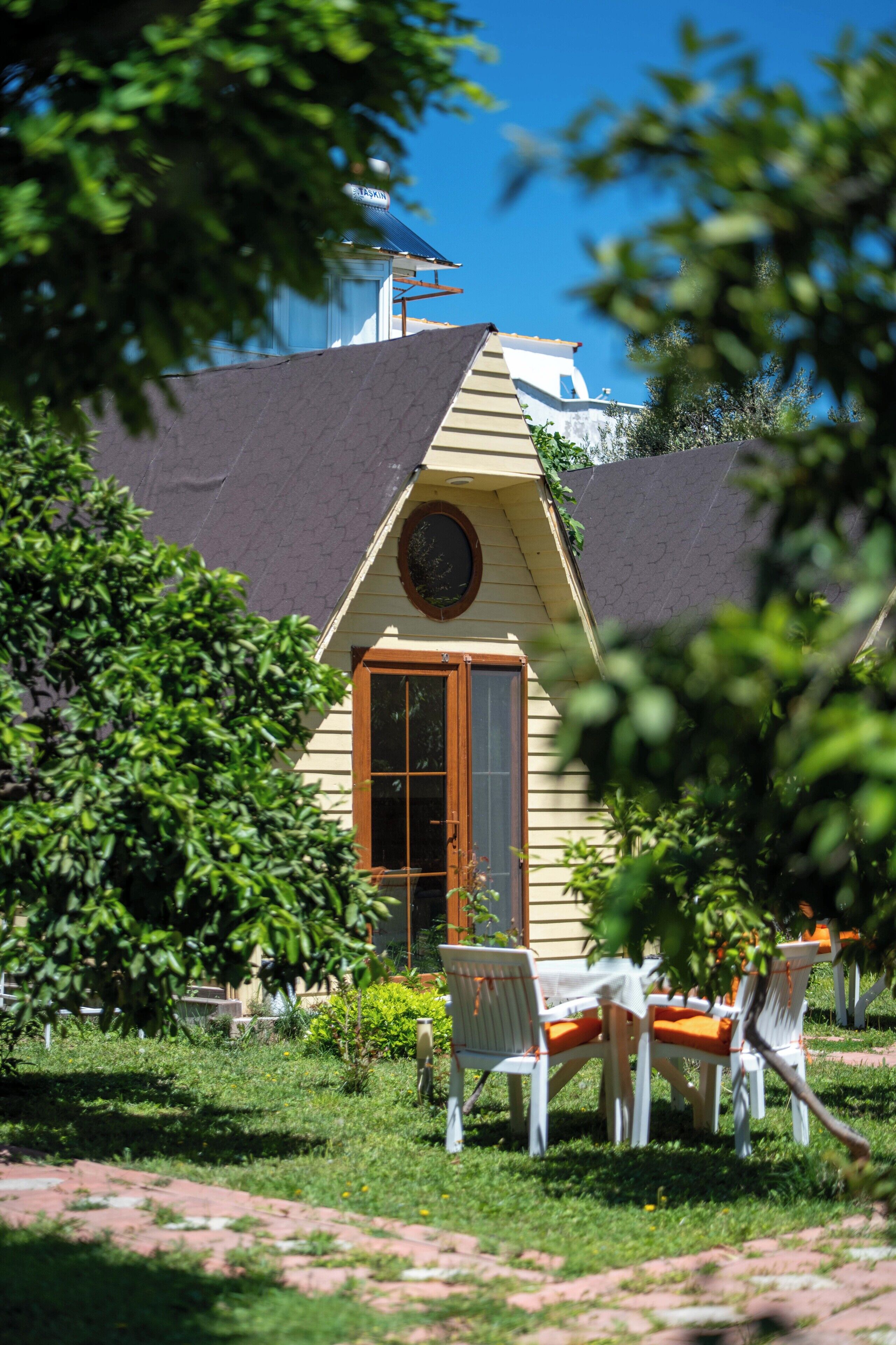 A cozy house with a garden, a dining area with chairs, and a large window.