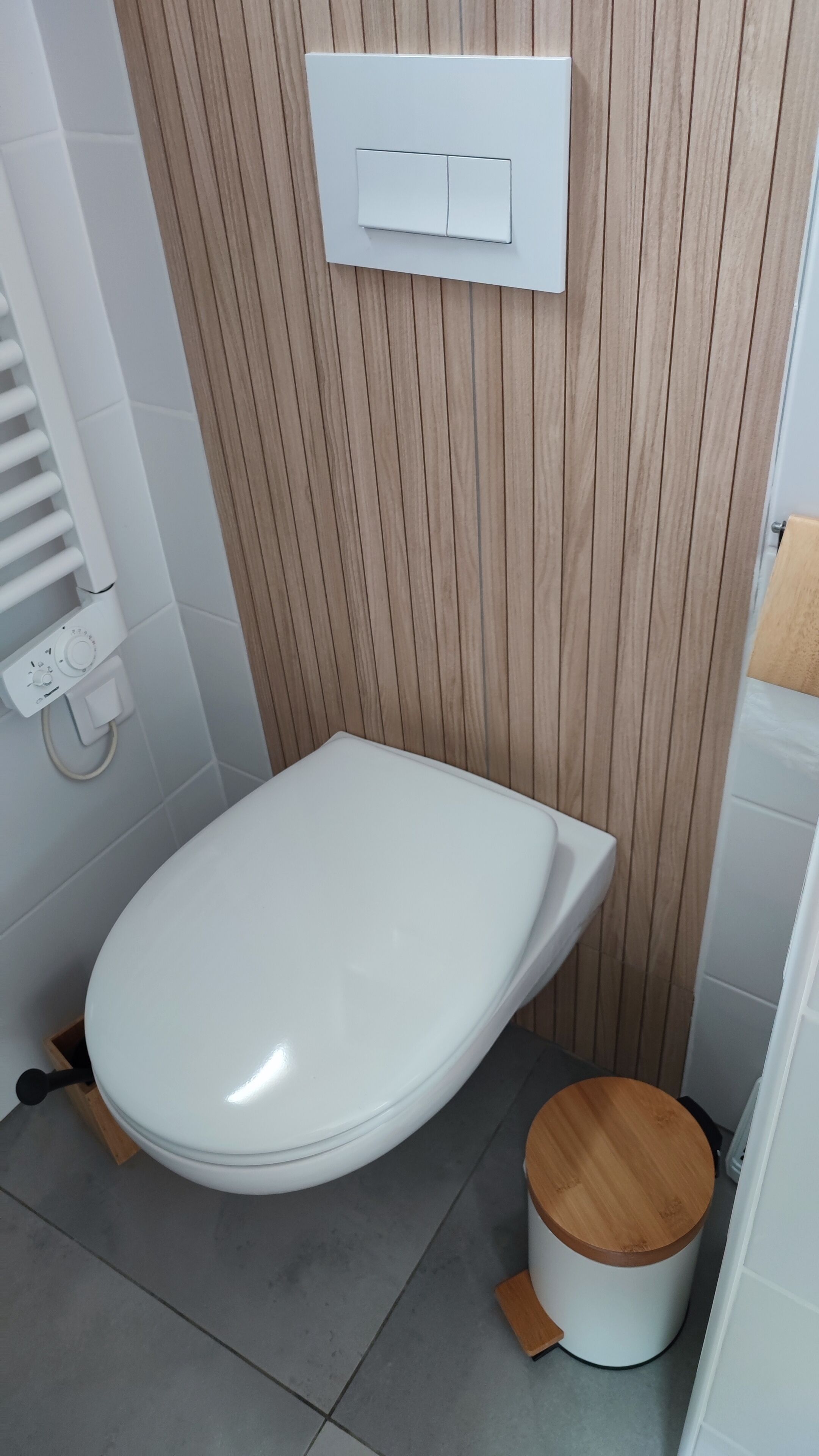 Een moderne badkamer met een wit toilet, een houten wandpaneel en een witte spoelbak.