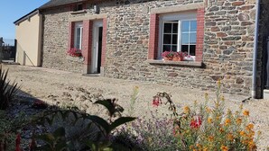Una casa de piedra con dos ventanas, cada una con un persiano rojo y macetas con flores.